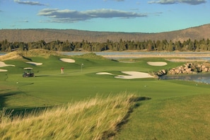 A golf course with sand bunkers, a water hazard, and a distant forested hill. - Klamath Falls | Nature Golf Retreat | Pool + Golf | 3BR Sleeps 8 (Klamath Falls)