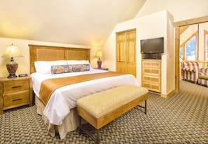 Une chambre d’hôtel avec un lit, des lampes de chevet, une télévision, un banc, une armoire et une vue sur l’extérieur, visible à travers une porte.
