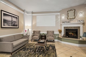 Un salon comprenant un canapé, deux fauteuils, une table basse, une cheminée, un tableau encadré et un miroir décoratif.
