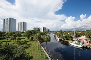 A canal with boats, a grassy area with trees, and high-rise buildings in the background. - Santa Barbara | Romantic Beach Retreat | Pool + Beach (Pompano Beach)