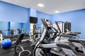 A gym with exercise equipment, a television, and a blue wall. - Santa Barbara | Romantic Beach Retreat | Pool + Beach (Pompano Beach)