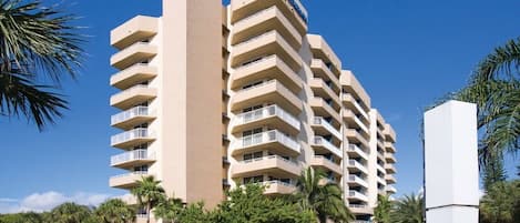 A multi-story hotel with balconies, palm trees, and a clear sky.
