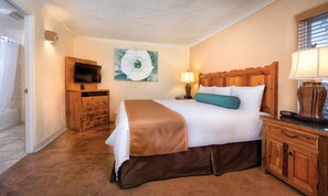 Quarto de hotel com uma cama, televisão, pintura, luminária e um armário de madeira.