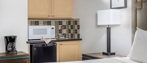 A compact hotel room with a bed, a small kitchenette with a microwave, a sink, and a coffee maker.
