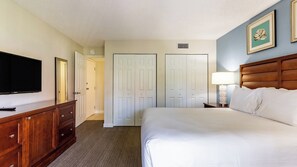 A hotel room with a bed, a TV, a dresser, and a door leading to another room. - Pompano Beach | Tranquil Poolside Stay | Pool + Beach (Pompano Beach)