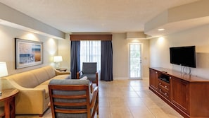 A hotel room with a sofa, armchairs, a TV, a lamp, a painting, and a window with curtains. - Pompano Beach | Tranquil Poolside Stay | Pool + Beach (Pompano Beach)