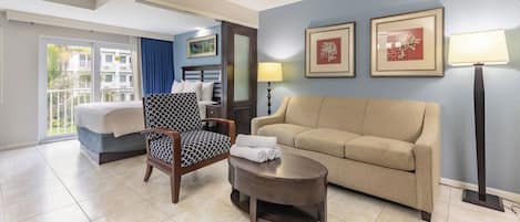 A hotel room with a bed, a chair, a sofa, a table, and two framed pictures on the wall.