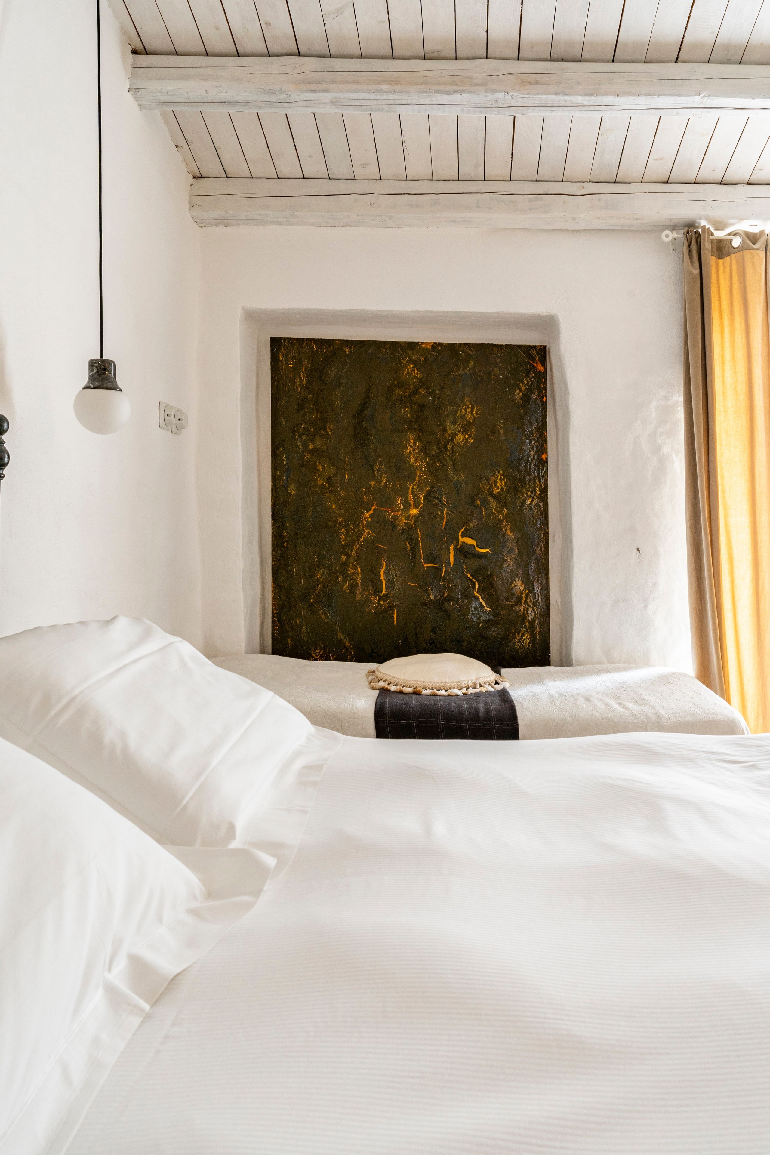 Ein Schlafzimmer mit einem Bett, einer Wandleuchte und einem Fenster mit Vorhängen.