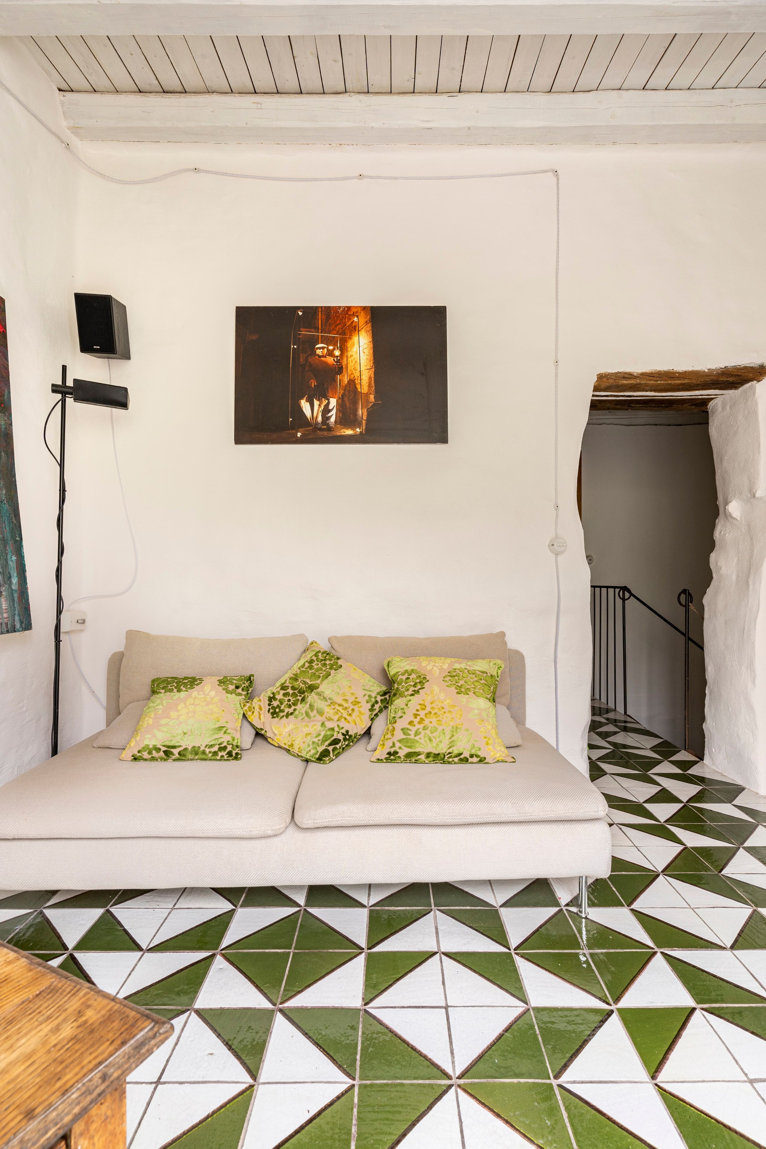 A room with a sofa, a painting, a speaker, and a patterned floor.