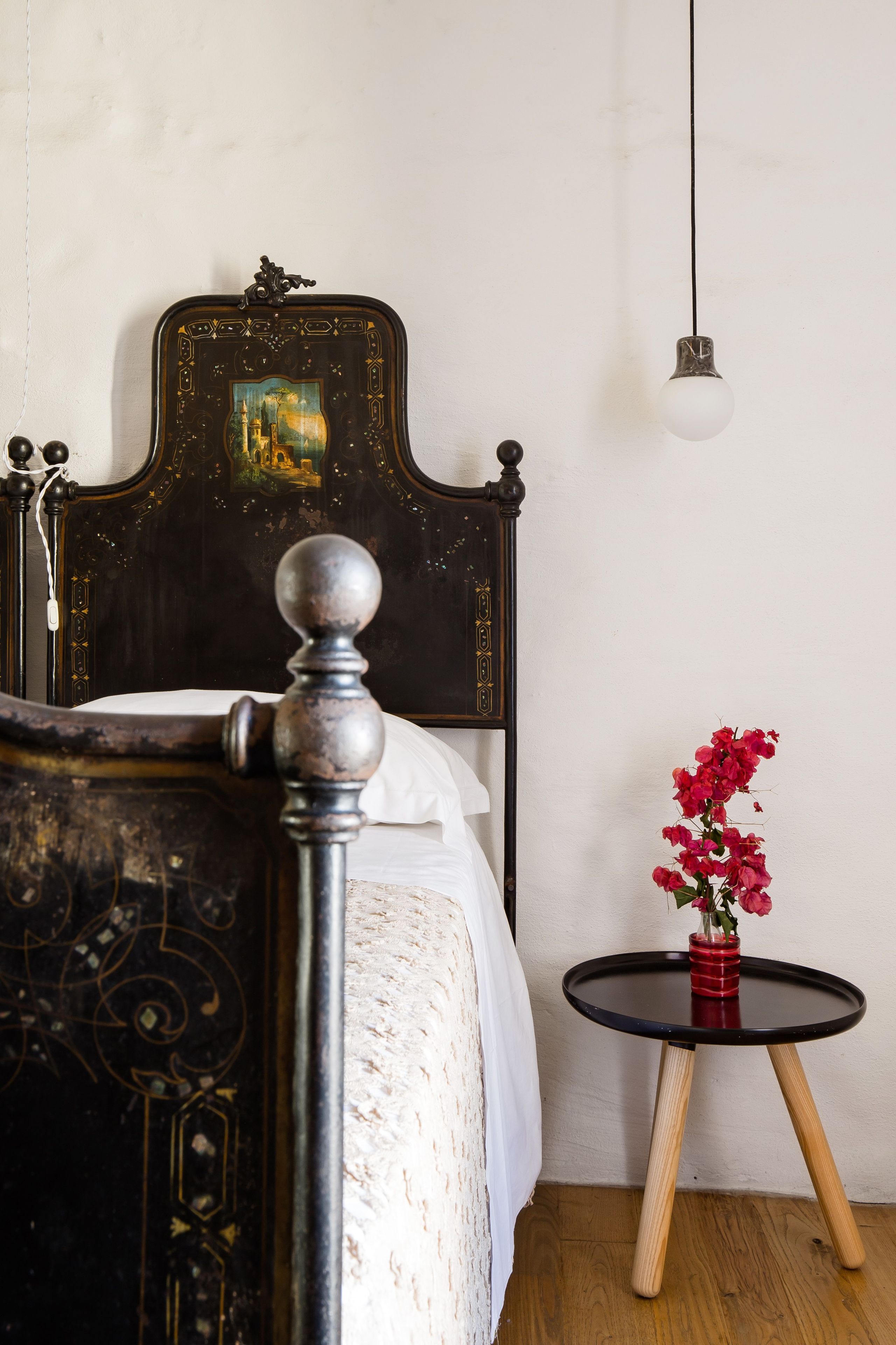 A bed with a dark headboard and a decorative design, a bedside table with a vase of flowers, and a hanging light fixture.