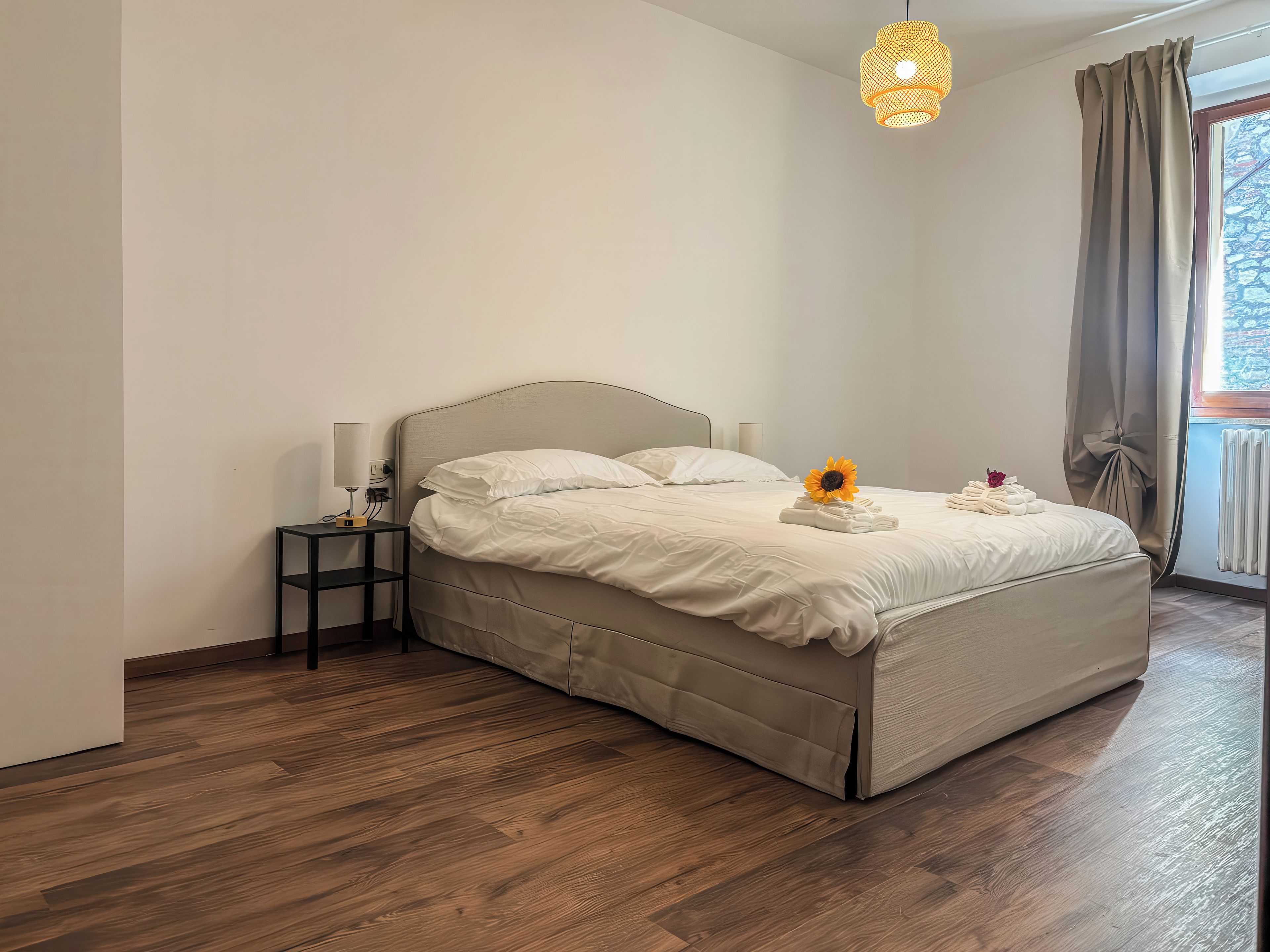 A neatly made bed with a headboard, a bedside table with a lamp, and a window with curtains.