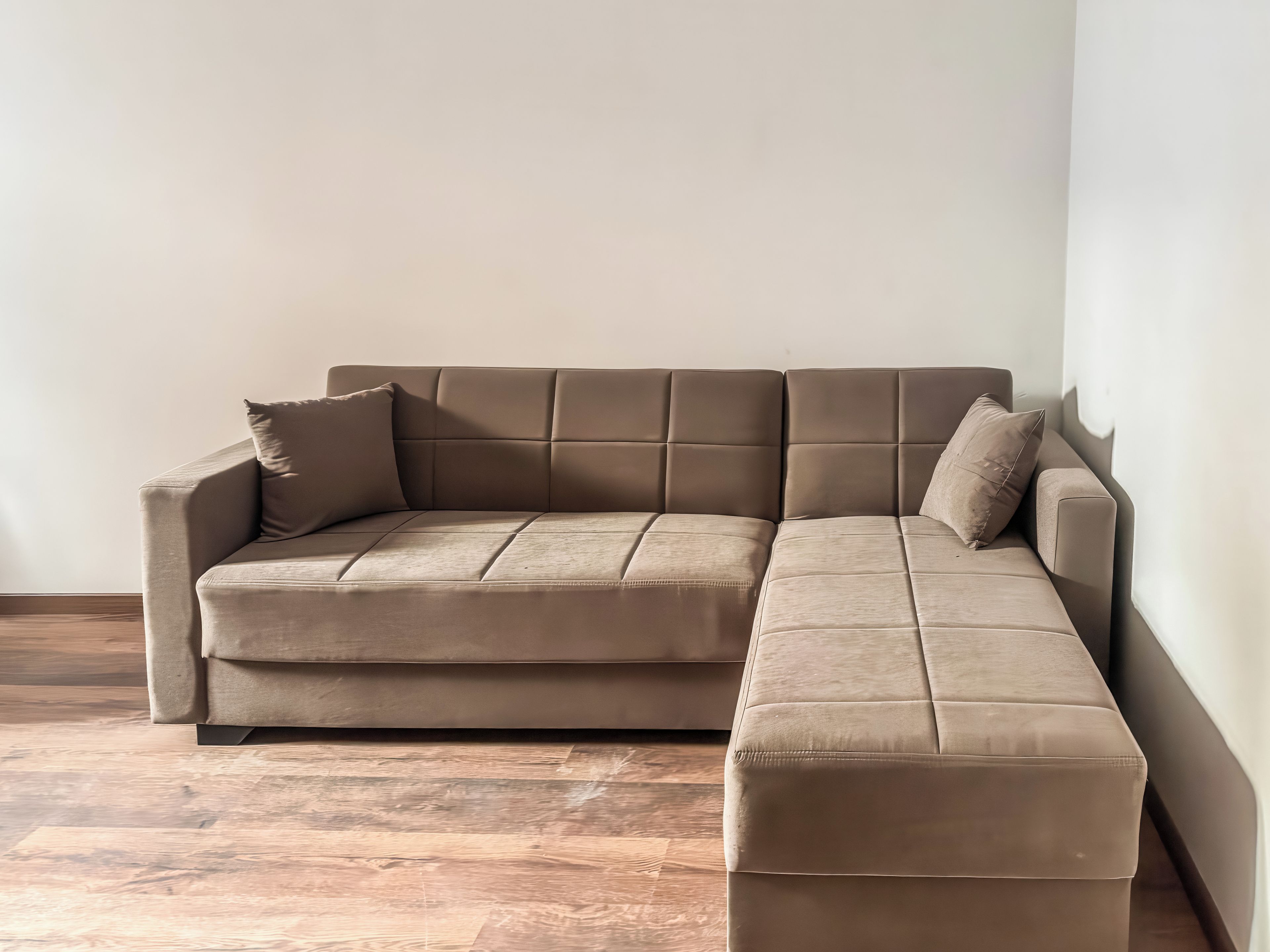 Ein Ecksofa mit Chaiselongue, vor einer schlichten Wand auf Holzboden.
