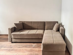 A sectional sofa with a chaise, positioned against a plain wall, on a wooden floor.