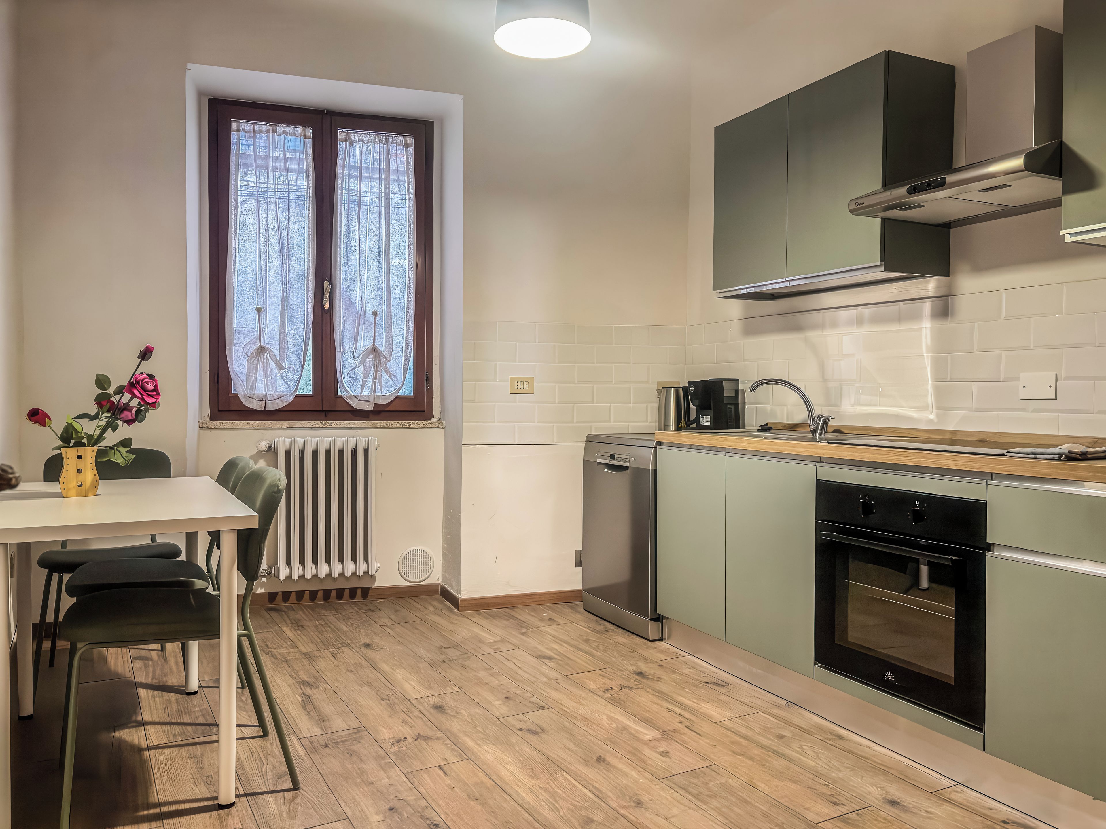 A modern kitchen with a built-in dishwasher, oven, and a window with curtains.