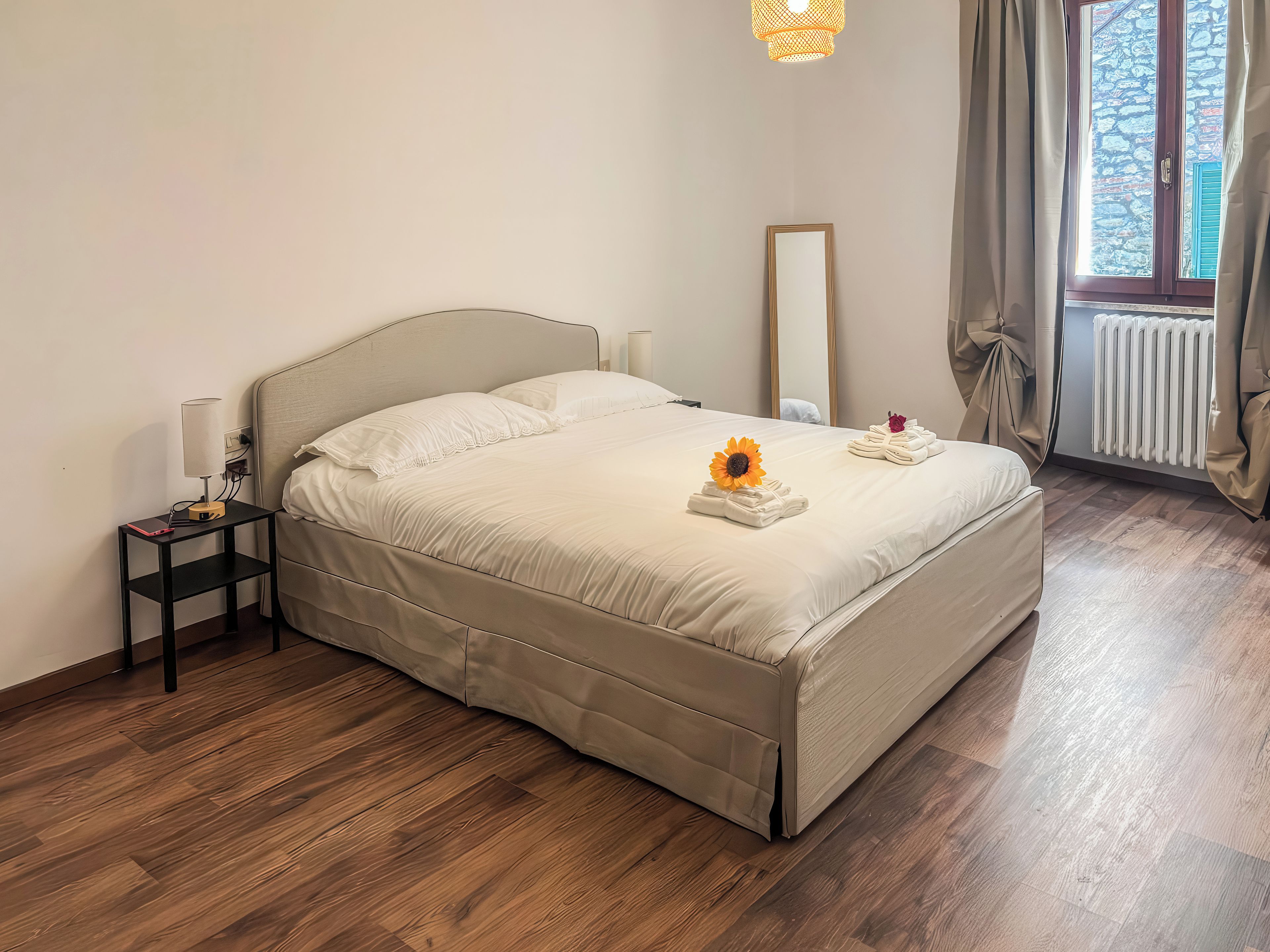 Una cama bien hecha con cabecera, una mesita de noche con lámpara y una ventana con cortinas.