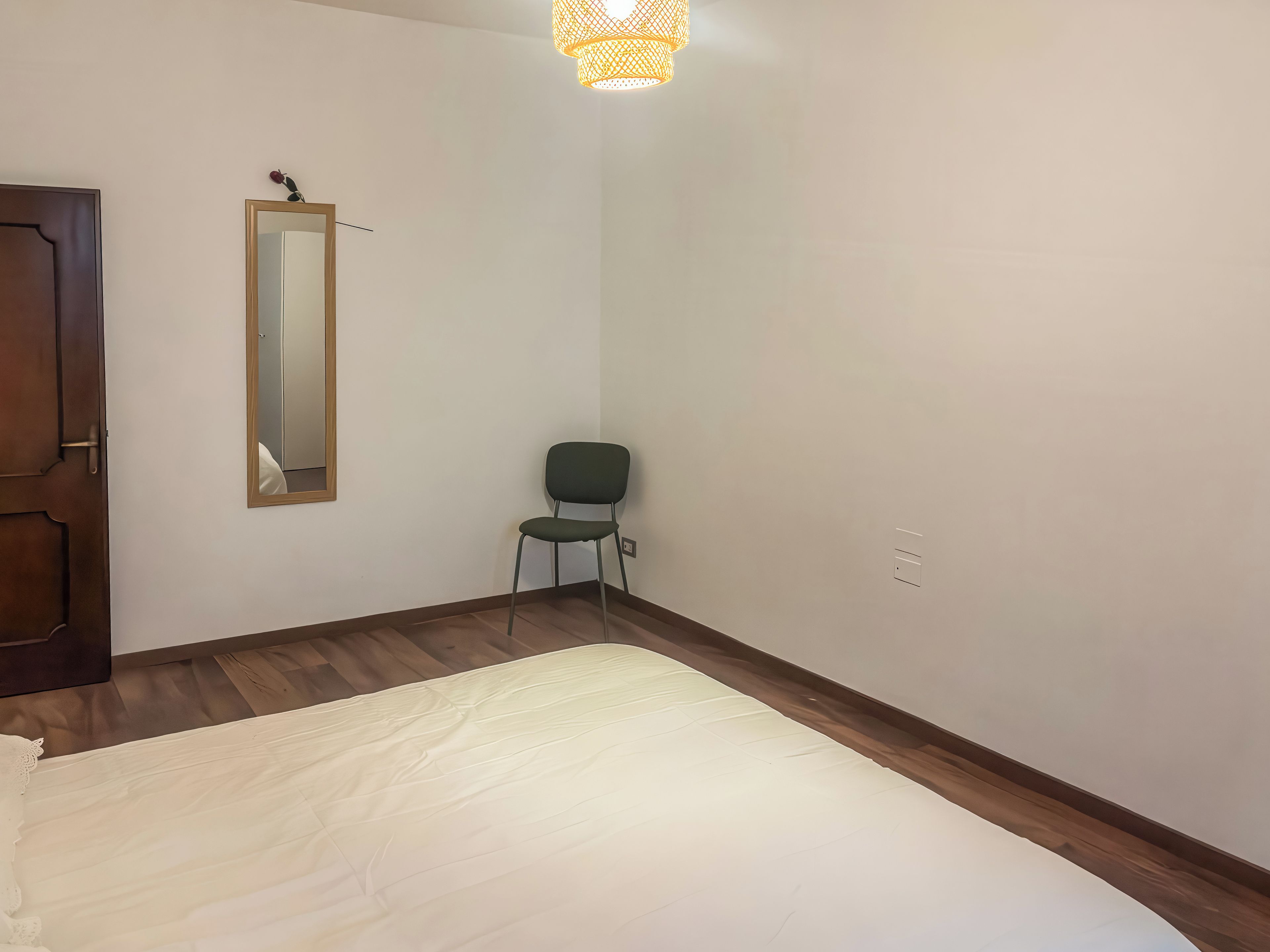 A bedroom with a bed, a chair, a mirror, and a door.