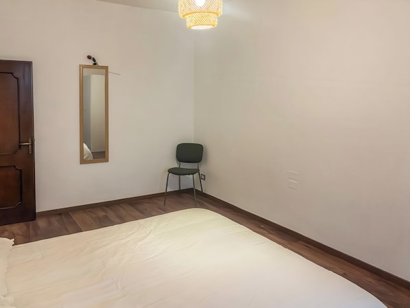 A bedroom with a bed, a chair, a mirror, and a door.