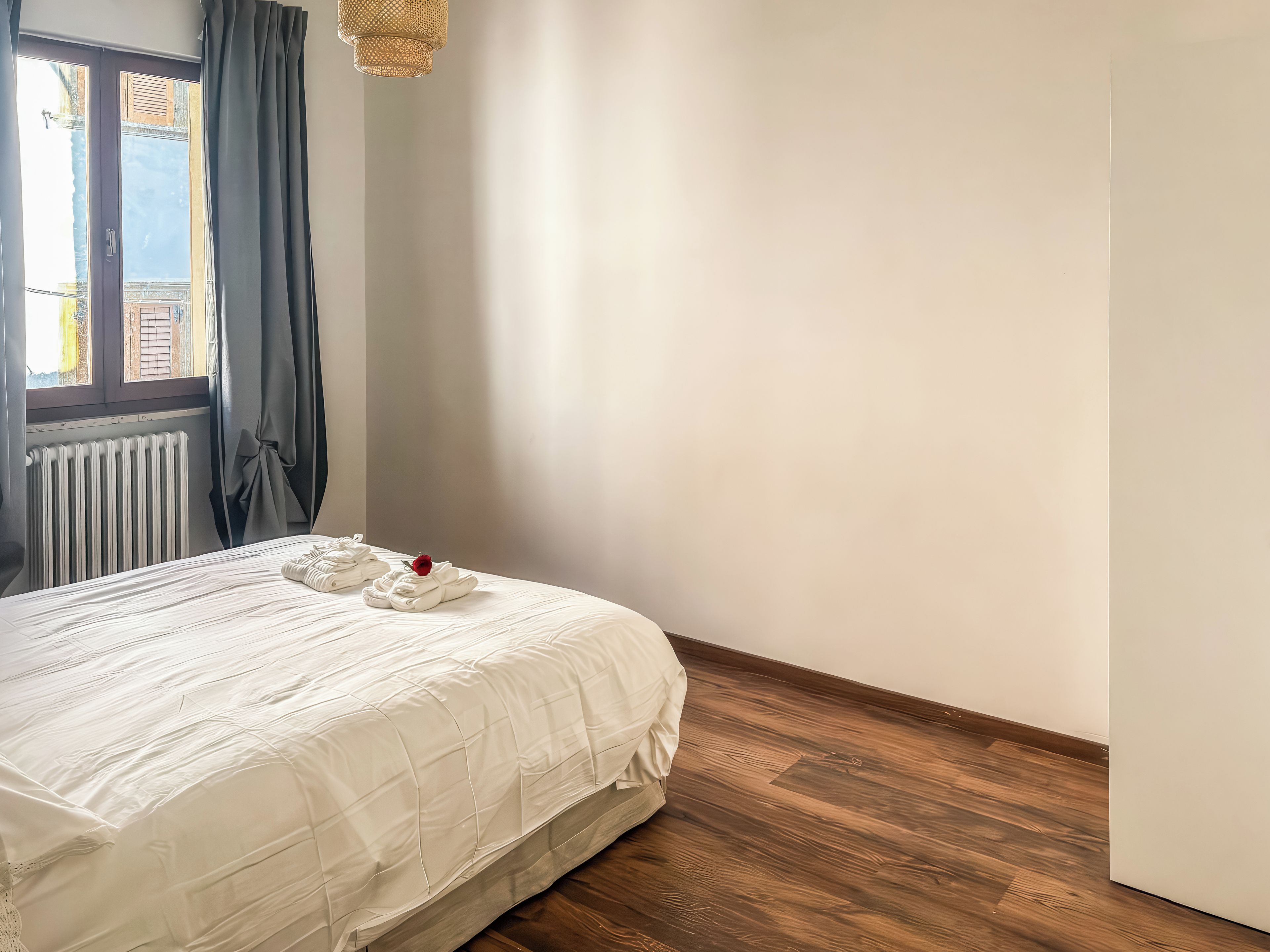 Habitación de hotel con cama, radiador y ventana con cortinas.