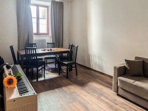 A dining area with a wooden table and chairs, a piano, and a sofa.