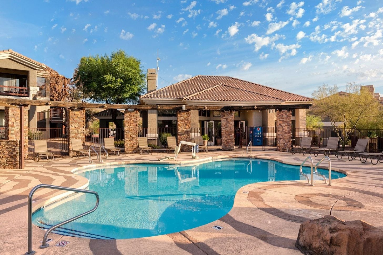 A pool area with a clear blue pool, lounge chairs, and a covered seating area.