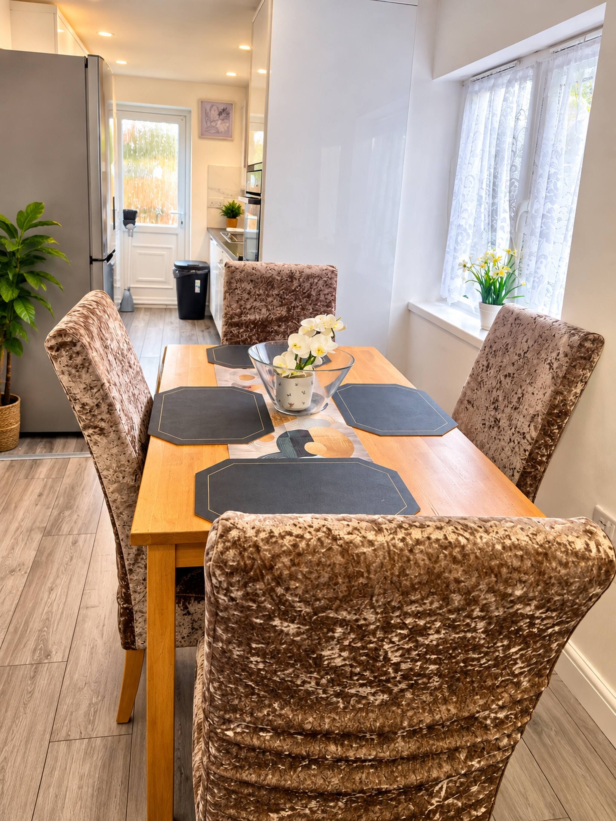 A dining area with a wooden table, patterned chairs, and a vase with flowers.