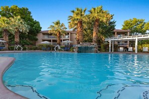 Piscina con palmeras y una cascada, rodeada de sillas de descanso y sombrillas.