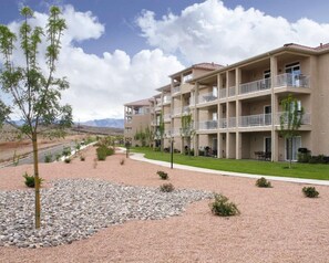Un hotel de varios pisos con balcones, un patio ajardinado y vistas a las montañas.