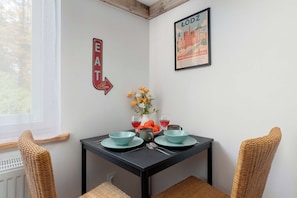 Un comedor con una mesa dispuesta para dos, dos sillas, un jarrón con flores y un cuadro en la pared.