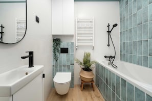 Un baño moderno con inodoro blanco, lavabo negro, ducha con cabezal de mano y una planta en maceta.