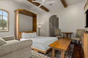 Quarto de hotel com cama, escrivaninha, poltrona, sofá e televisão.