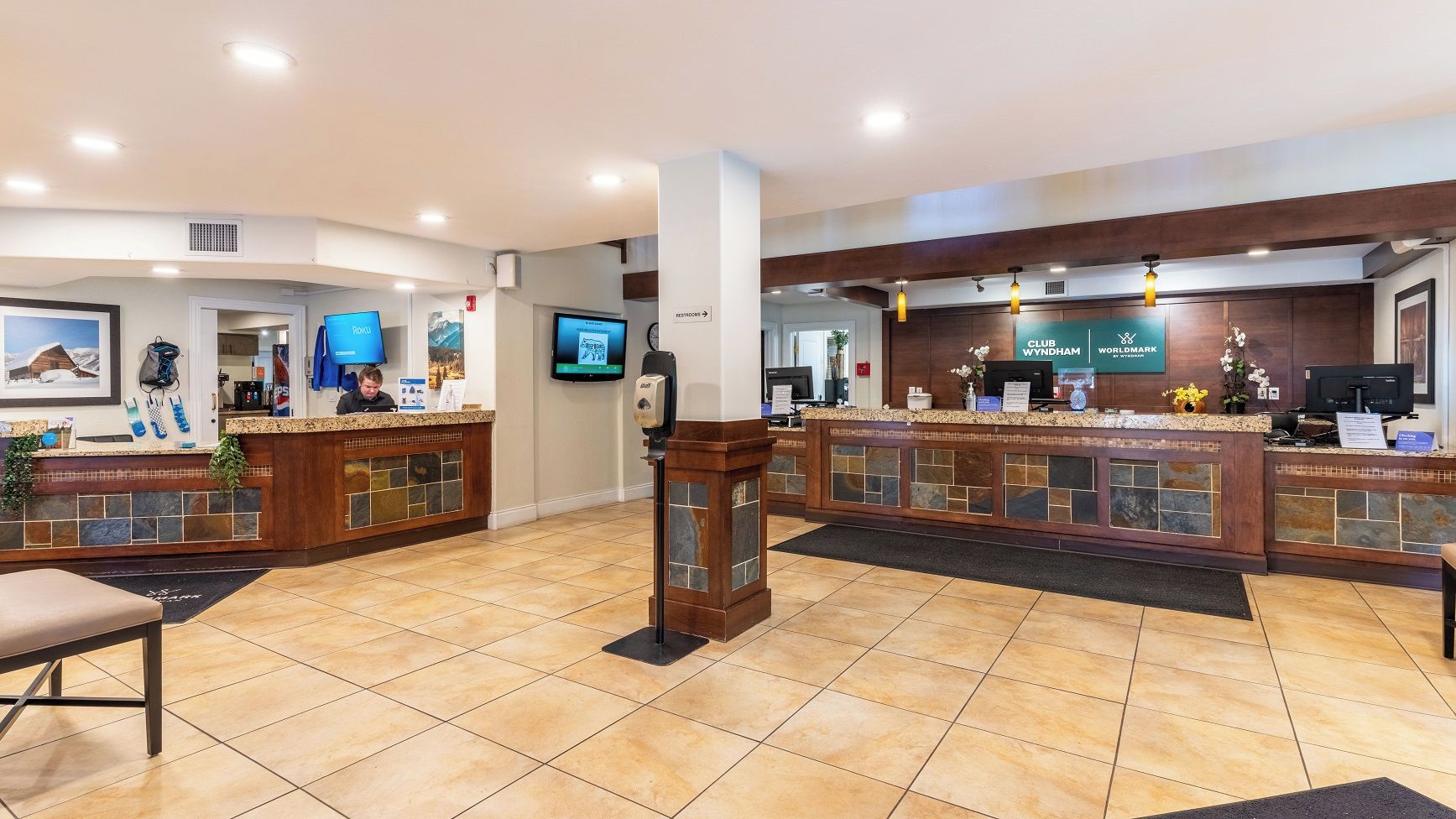 Un espace d’accueil d’hôtel comprenant deux comptoirs, une horloge et un écran de télévision.