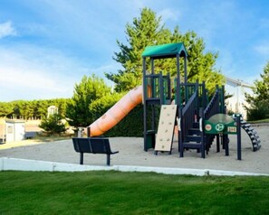 Une aire de jeux avec un toboggan, des structures d’escalade et un banc.