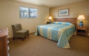 A bedroom with a bed, two nightstands, a chair, a desk, and a window with blinds. - Ocean Park | Cozy Beach Retreat | Pool + Beach (Ocean Park)