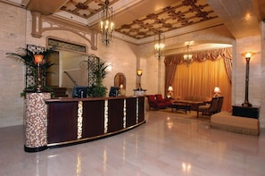 Un vestíbulo con mostrador de recepción, zona de estar y elementos decorativos como plantas y candelabros.