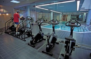 Ein Fitnessraum mit Trainingsgeräten, einem Schwimmbad und einer Person, die ein Laufband benutzt.