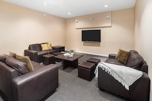 Ein modernes Wohnzimmer mit Fernseher, Ledersofas, einem Couchtisch und einem gemusterten Teppich.
