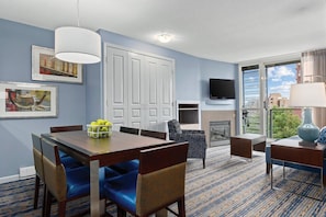 Quarto de hotel com mesa de jantar, cadeiras, televisão, lareira e uma grande janela com vista.