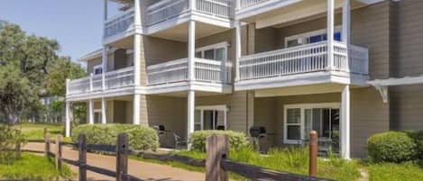 A multi-story building with balconies, a paved walkway, and a landscaped area with mulch and plants.