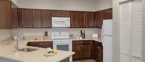 A compact kitchen with dark wooden cabinets, a white microwave, a stove, and a refrigerator.