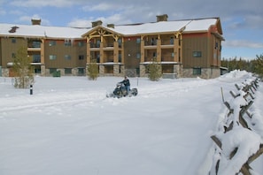 Een meerhoog gebouw met een sneeuwbedekt dak en een persoon die op een sneeuwscooter rijdt op de voorgrond.