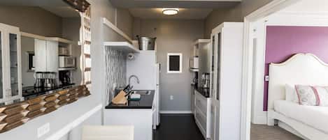 A compact hotel room with a kitchenette, a dining area, and a bed.