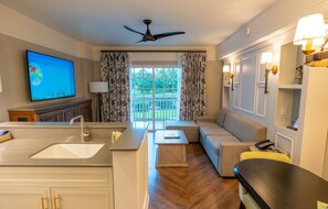 A modern hotel room with a kitchen area, a seating area with a sofa and armchairs, a flat-screen TV, and a balcony with curtains. - Orlando | Relaxing Disney Retreat | Pool + Spa (Lake Buena Vista)
