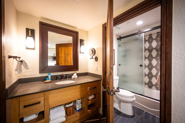A bathroom with a wooden vanity, a large mirror, a toilet, and a glass shower enclosure. - Orlando | Family Lodge Retreat | Pool + Hot Tub | 2BR (Lake Buena Vista)