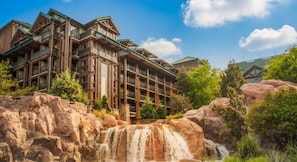 A multi-story building with a wooden facade and balconies, situated in a natural setting with a waterfall and rocky terrain. - Orlando | Family Lodge Retreat | Pool + Resort | 2BR (Lake Buena Vista)