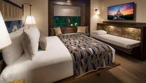 Ein Hotelzimmer mit einem großen Bett, einem kleineren Bett, einem Nachttisch, einer Lampe und einem am Wand montierten Fernseher.