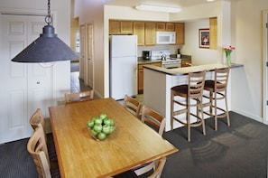 Een compacte keuken met houten kastjes, een magnetron, een fornuis en een klein eiland met barstoelen.