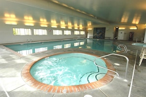 Een binnenzwembad met een whirlpool, betegelde wanden en een wand met ramen.
