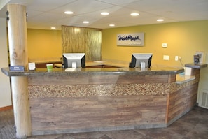 Ein Empfangstresen mit Holzdesign, zwei Computermonitore und ein Schild mit der Aufschrift 'Welcome Mark by Wyndham'.
