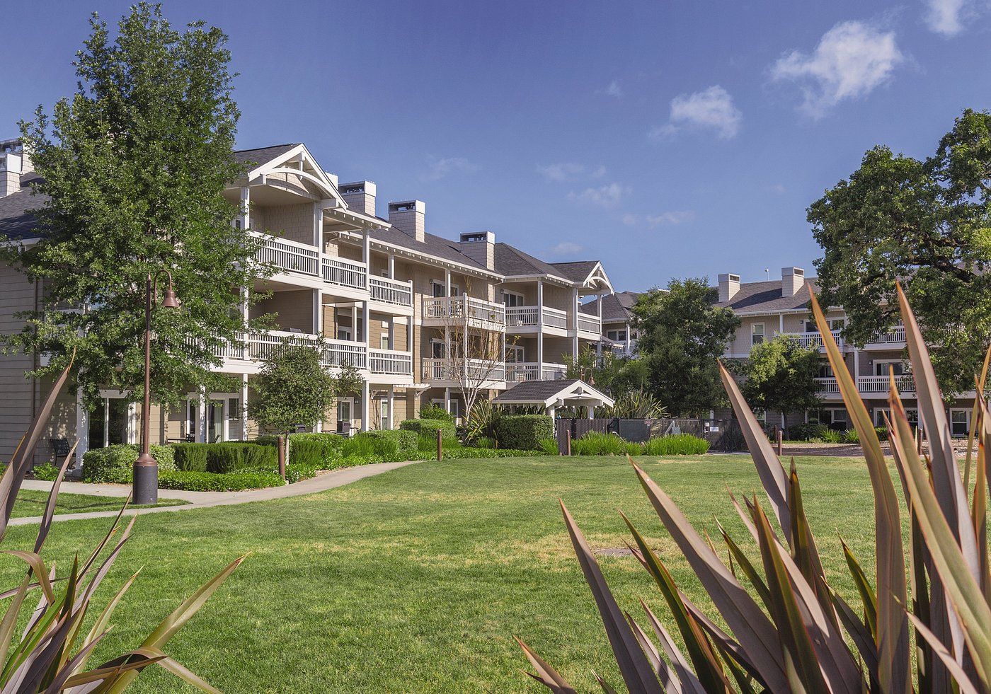 A multi-story residential building with balconies, a well-maintained lawn, and surrounding greenery.