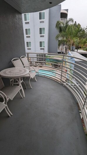 Un balcon avec une table ronde et des chaises, une piscine et, au fond, un bâtiment doté de nombreuses fenêtres.